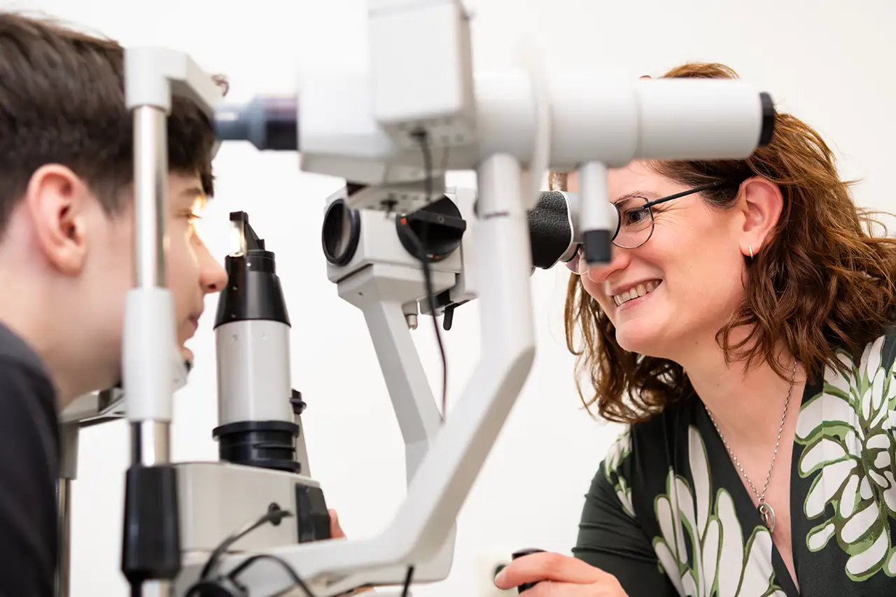 Augenoptikermeisterin Britta Nausch führt mit einer Spaltlampe eine augenoptische Untersuchung bei einem jungen Mann durch